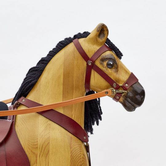 Hlava houpacího koně s koženým postrojem a vlněnou hřívou